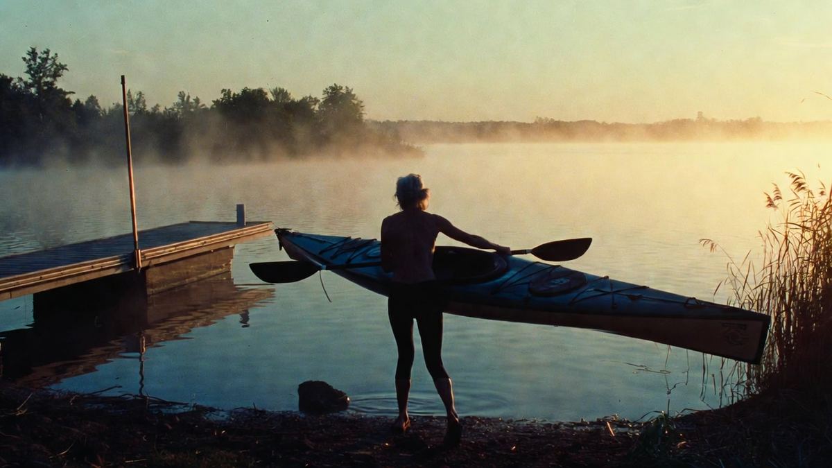 A woman carrying a kayak to the water's edge on a misty morning lake